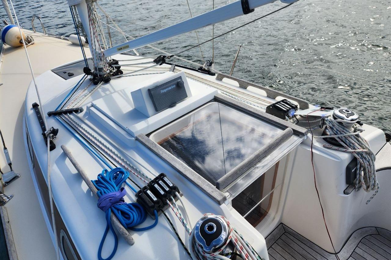Sailboat deck of 2017 Rustler 33 with rigging and hatch, on calm water.