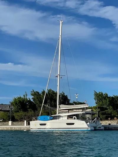  Yacht Photos Pics 2019 Fountaine Pajot Lucia 40 catamaran docked by lush greenery under a blue sky.