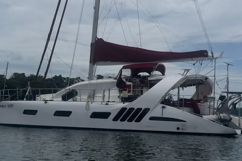 Manila Spirit Yacht Photos Pics Sailing catamaran Dean 5000, 2012 model, with maroon sails on calm water.
