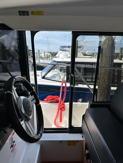 "freedom" Yacht Photos Pics Interior view of 2016 Jeanneau NC 14 boat, showing steering wheel and docked marina scene.