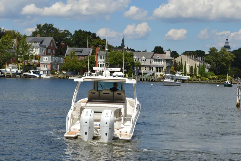 Station Break Yacht Photos Pics 2024 Tiara Yachts 34 LS cruising on a scenic waterfront with houses and boats.