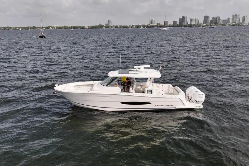 Yacht Photos Pics 2023 Regal 38 SAV boat cruising on a calm sea near a city skyline.