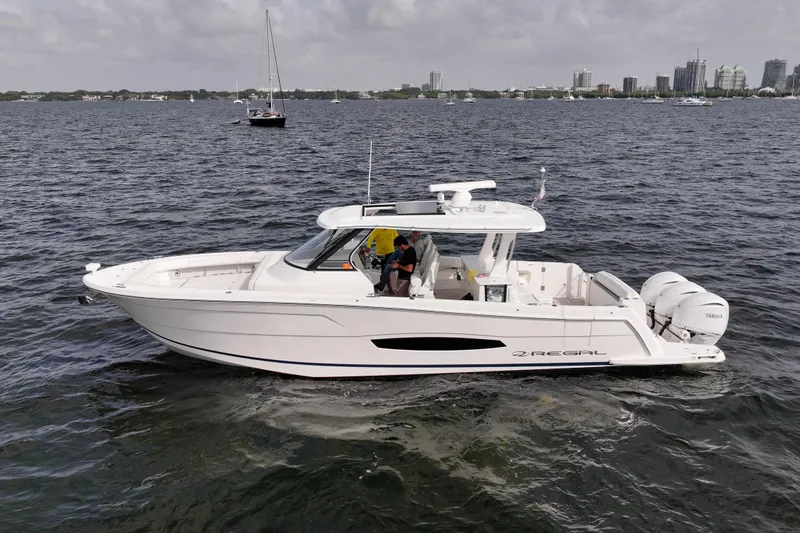  Yacht Photos Pics 2023 Regal 38 SAV boat cruising on a calm sea with city skyline in background.