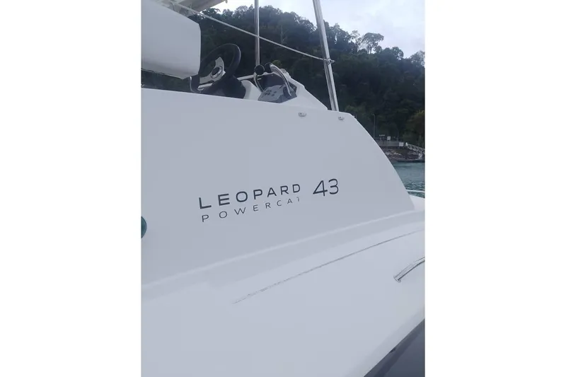  Yacht Photos Pics Leopard 43 Powercat boat with steering wheel, docked near lush greenery.