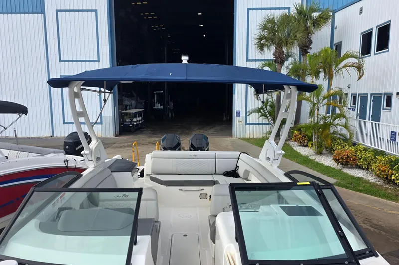  Yacht Photos Pics 2021 Sea Ray SDX 290 Outboard boat with blue canopy, docked near a warehouse.