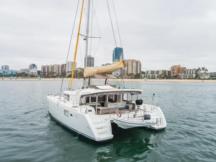 Limoncello Yacht Photos Pics 2016 Lagoon 450F catamaran sailing near urban coastline, overcast sky.