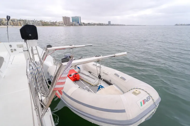 Limoncello Yacht Photos Pics Lagoon 450F catamaran with dinghy on calm water, cityscape in background, overcast sky.