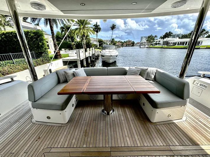 Journey Yacht Photos Pics Luxurious 2019 Sunseeker 76 Yacht deck with elegant seating and wooden table, docked by a scenic waterfront.