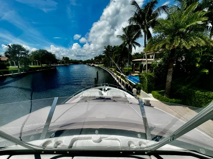 Journey Yacht Photos Pics 2019 Sunseeker 76 Yacht cruising along a scenic, palm-lined waterway under a bright blue sky.