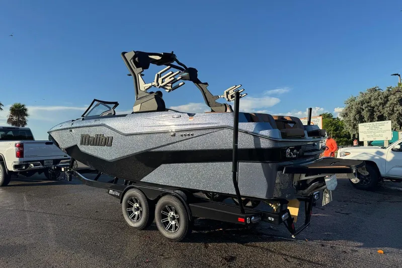  Yacht Photos Pics 2026 Malibu M230 boat on trailer, parked outdoors under clear blue sky.