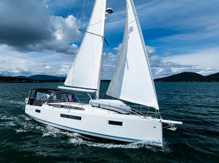 Into The Blue Yacht Photos Pics 2022 Jeanneau Sun Odyssey 410 sailing on a scenic lake under a partly cloudy sky.
