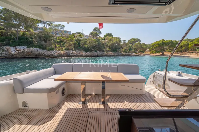 One Step Closer Yacht Photos Pics Luxurious 2024 Prestige 590 yacht deck with seating, table, and scenic coastal view.