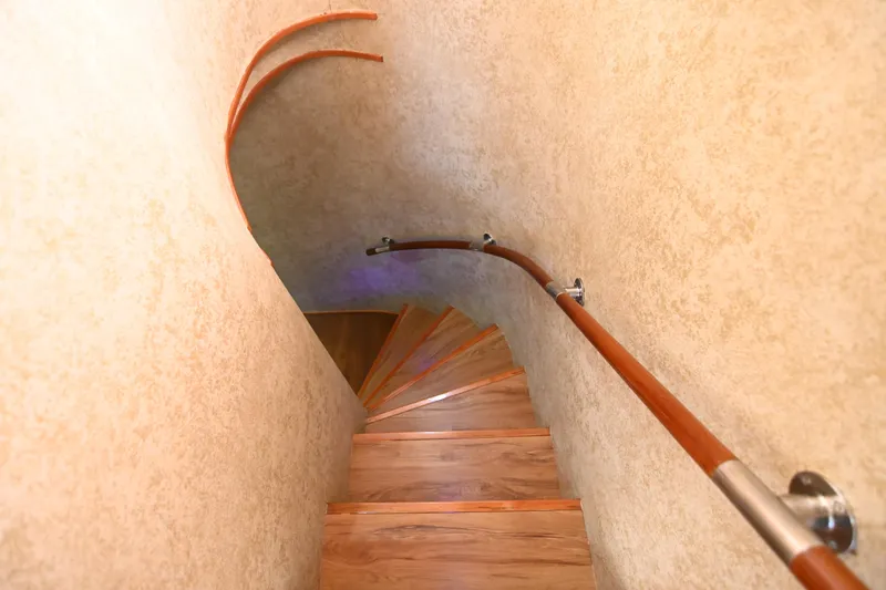  Yacht Photos Pics Spiral wooden staircase with curved handrail in a narrow, beige-walled space.