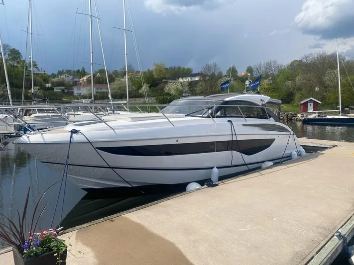 V40157 Yacht Photos Pics 2023 Princess V40 yacht docked at a marina, surrounded by calm water and greenery.