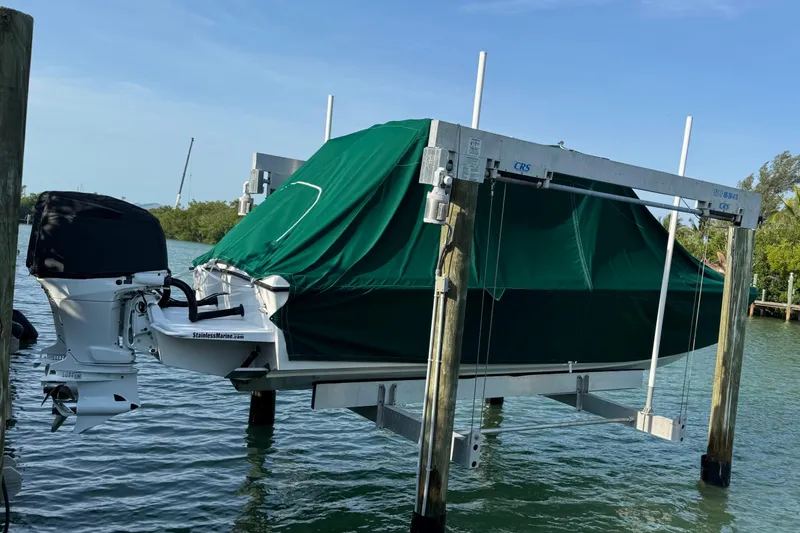  Yacht Photos Pics 2022 Whitewater 28 Open boat with green cover on a lift over water.
