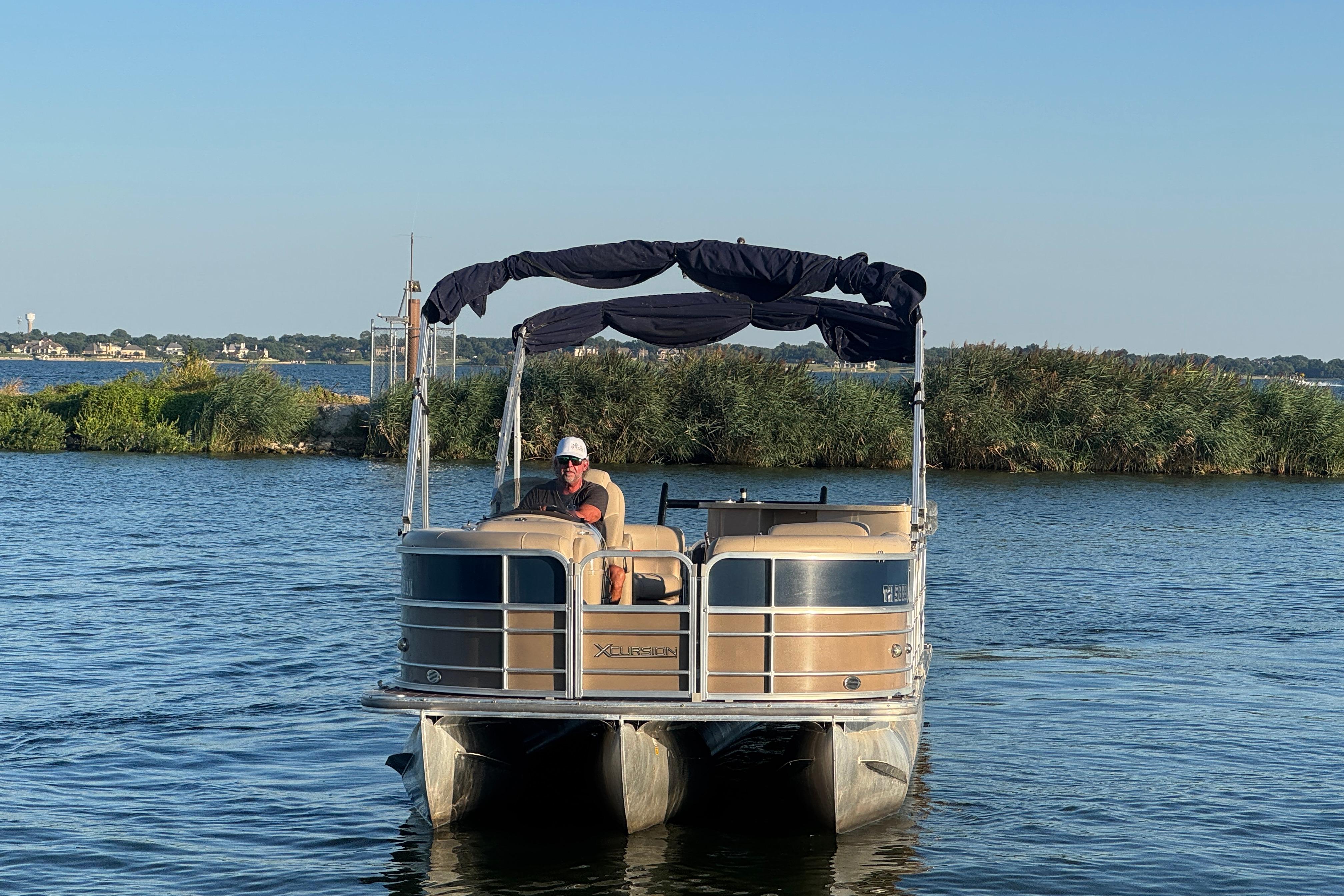 2016 Xcursion 23RFE pontoon boat on a serene lake with lush greenery.