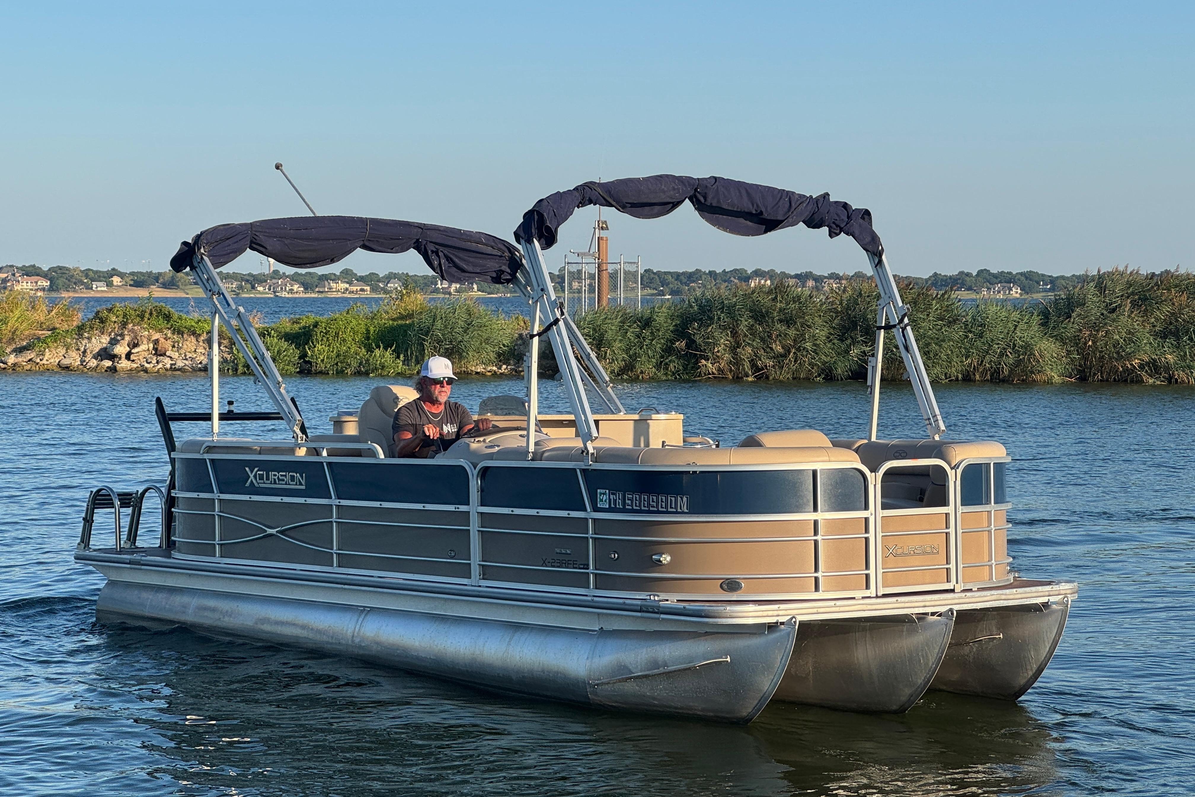 2016 Xcursion 23RFE pontoon boat on a serene lake with lush greenery.