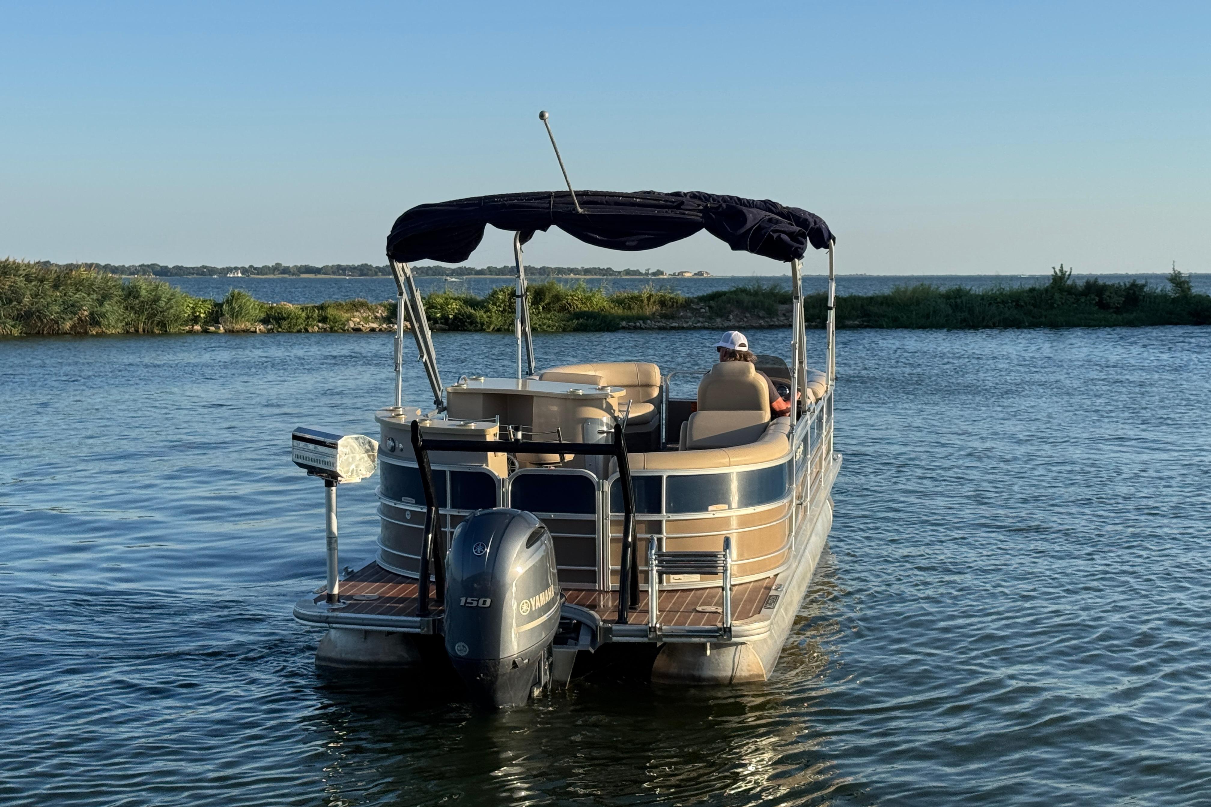 2016 Xcursion 23RFE pontoon boat on a serene lake with lush greenery.