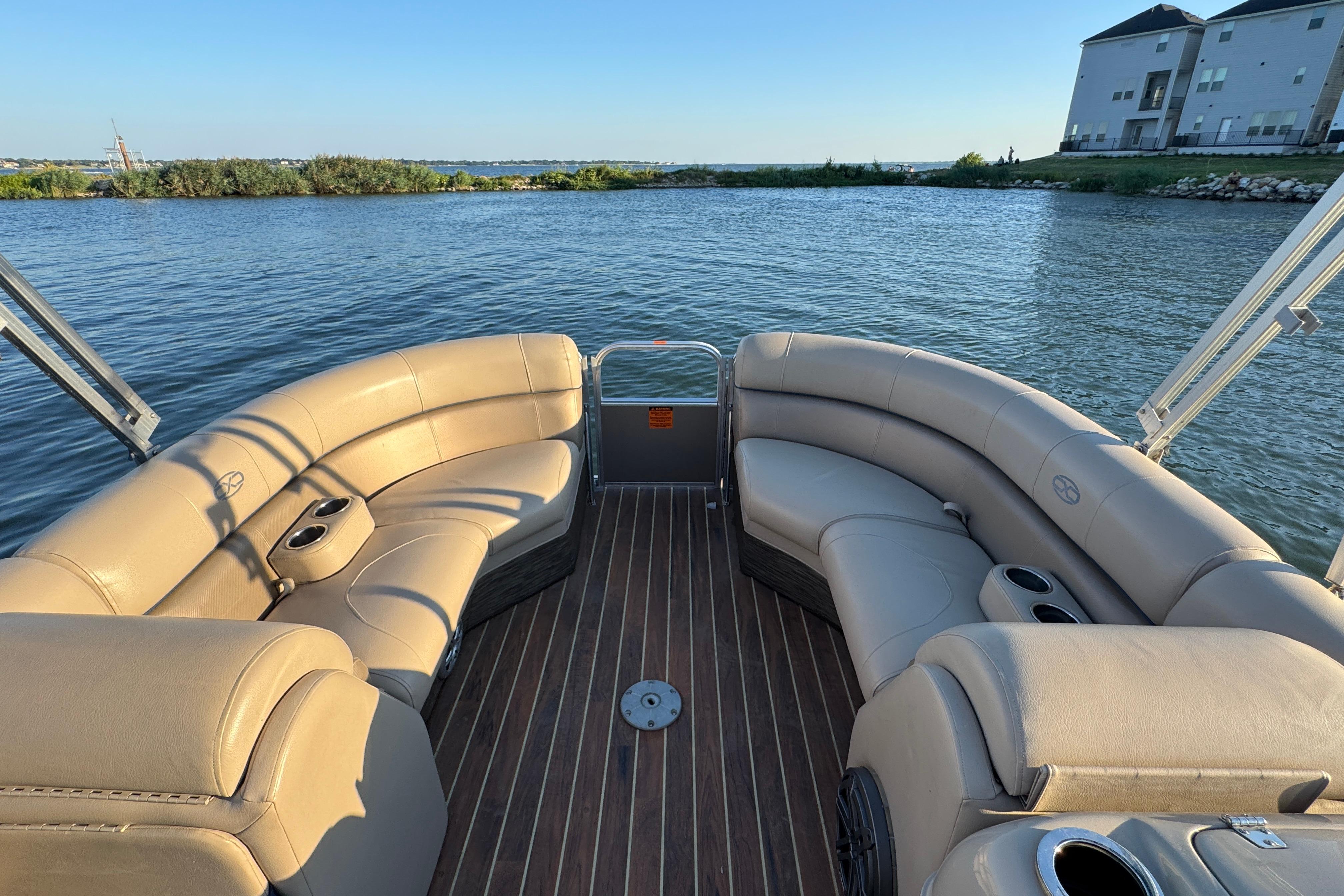 2016 Xcursion 23RFE pontoon boat with beige seating on a calm lake.