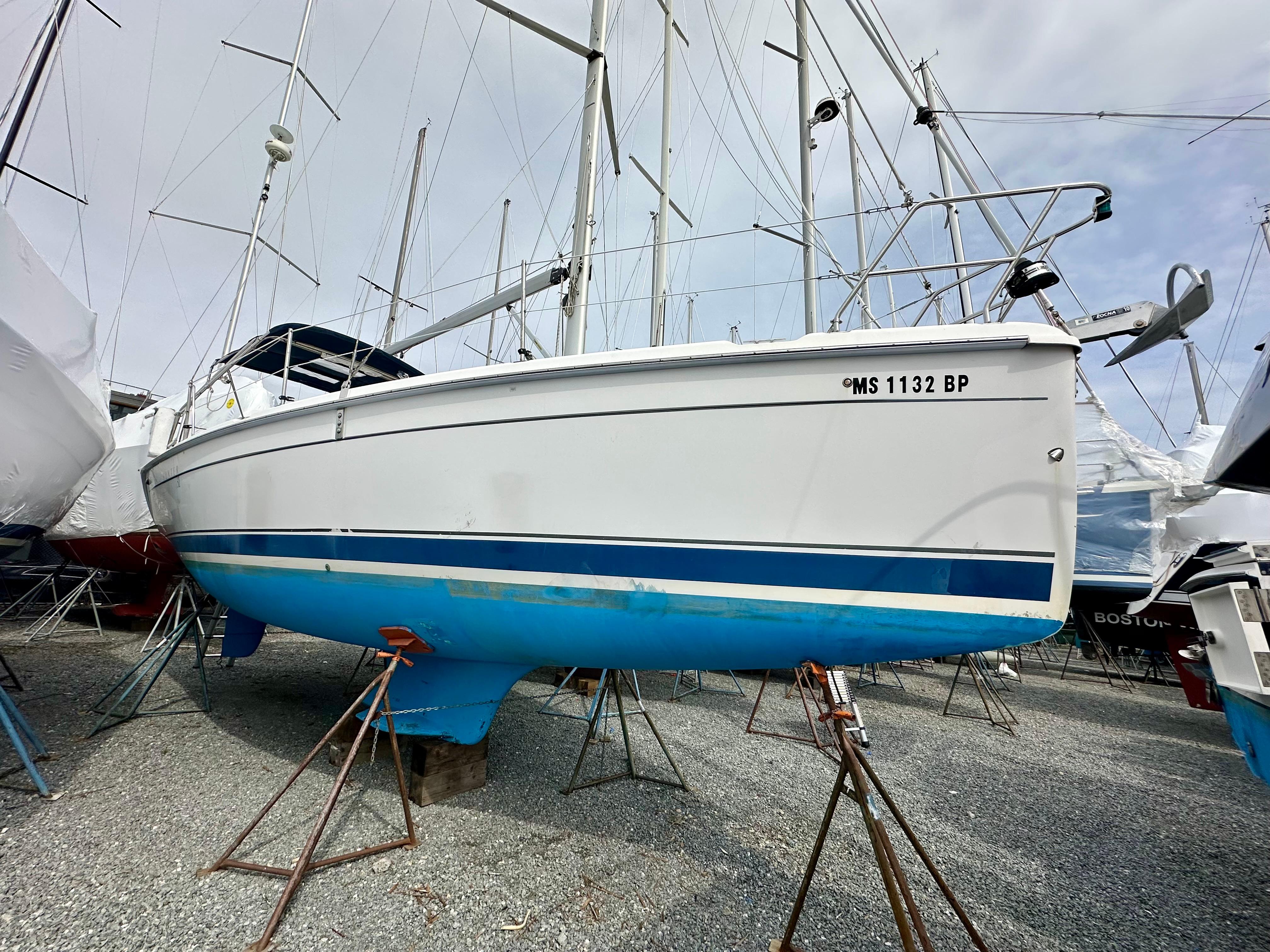 2006 Hunter 31 sailboat on stands, white hull with blue stripe, in a boatyard.