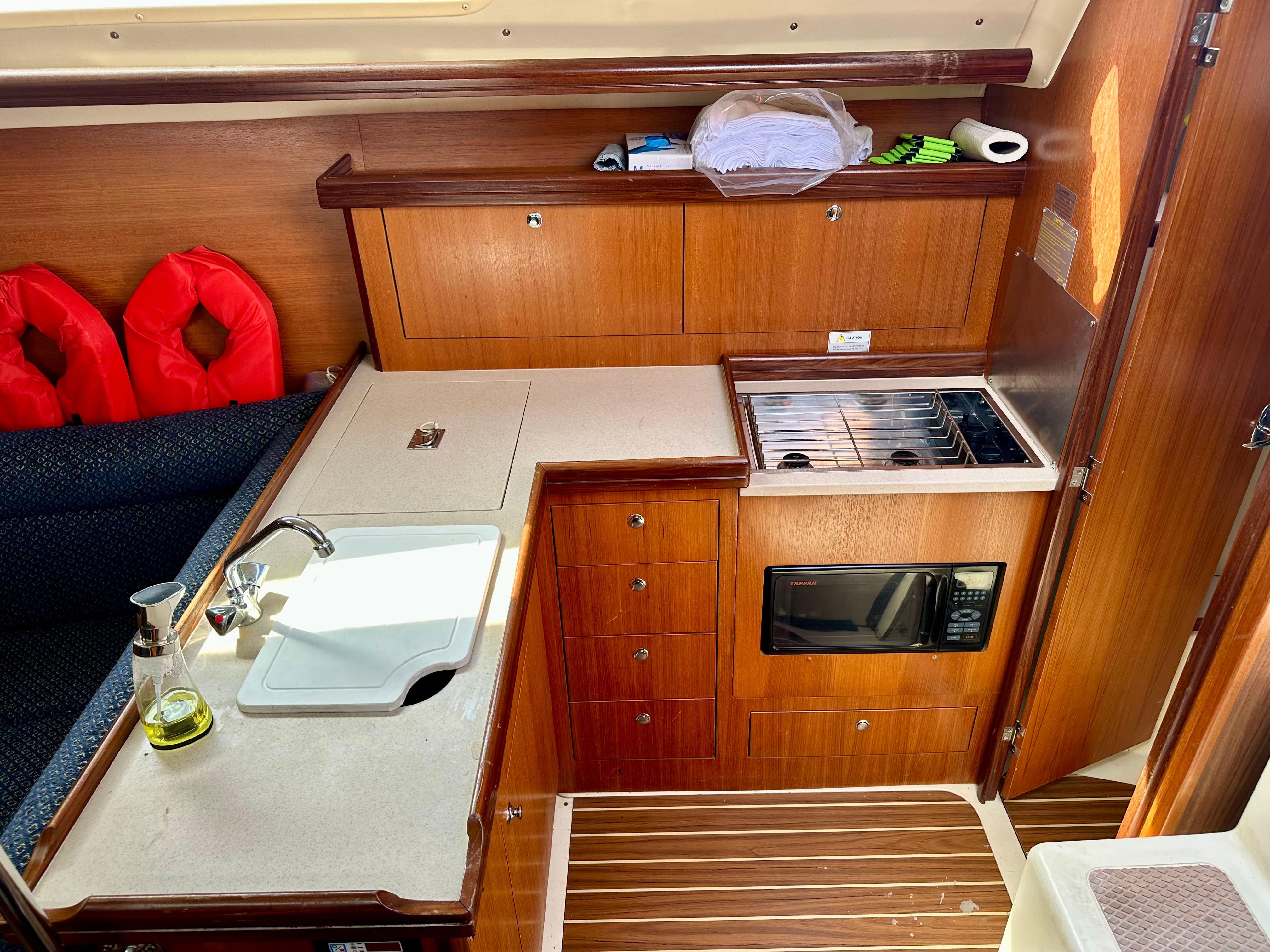 2006 Hunter 31 yacht interior kitchen with wooden cabinetry, sink, stove, and microwave.