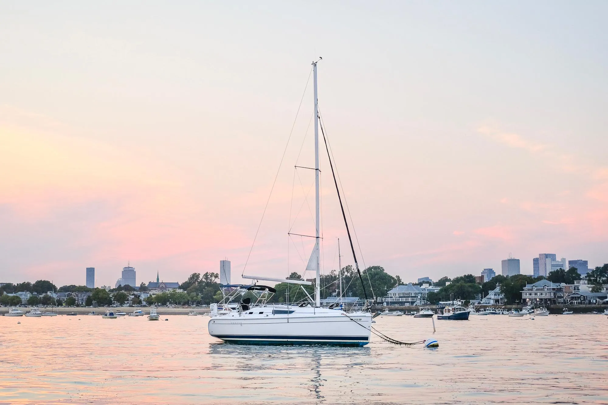 2006 Hunter 31 sailboat anchored at sunset with city skyline in background.