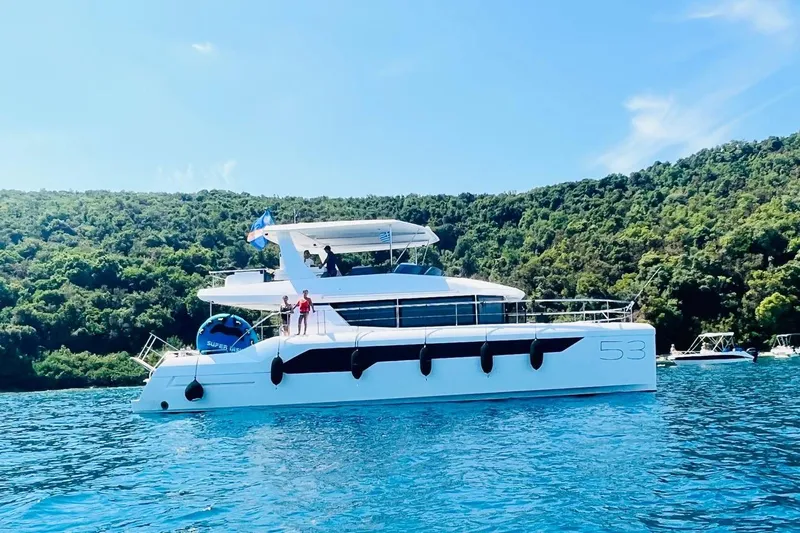  Yacht Photos Pics 2023 Leopard 53 Powercat yacht cruising on clear blue water near lush green shoreline.