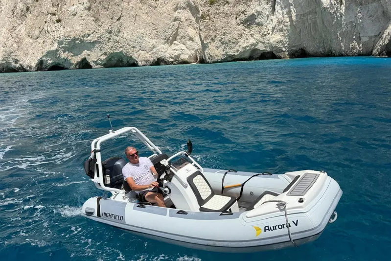  Yacht Photos Pics Man piloting a small boat on clear blue water near rocky cliffs.