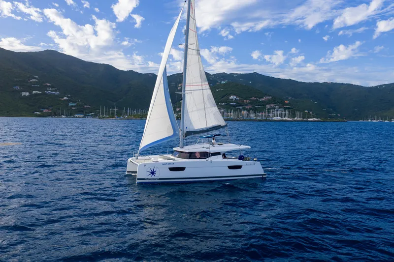 Nauti Mollie Yacht Photos Pics 2020 Fountaine Pajot Astrea 42 Catamaran sailing on blue ocean with mountainous backdrop.