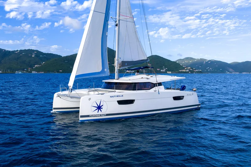 Nauti Mollie Yacht Photos Pics 2020 Fountaine Pajot Astrea 42 Catamaran sailing on blue ocean with scenic mountain backdrop.