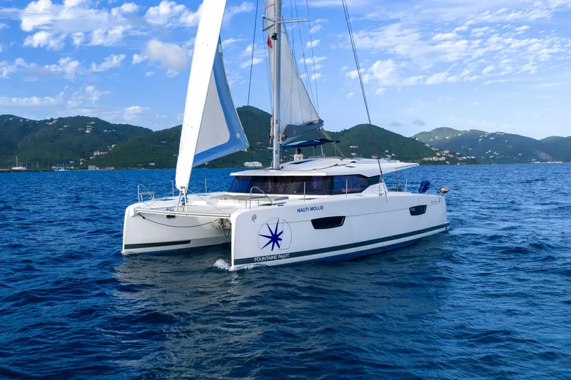 Nauti Mollie Yacht Photos Pics 2020 Fountaine Pajot Astrea 42 Catamaran sailing on blue ocean with scenic mountain backdrop.