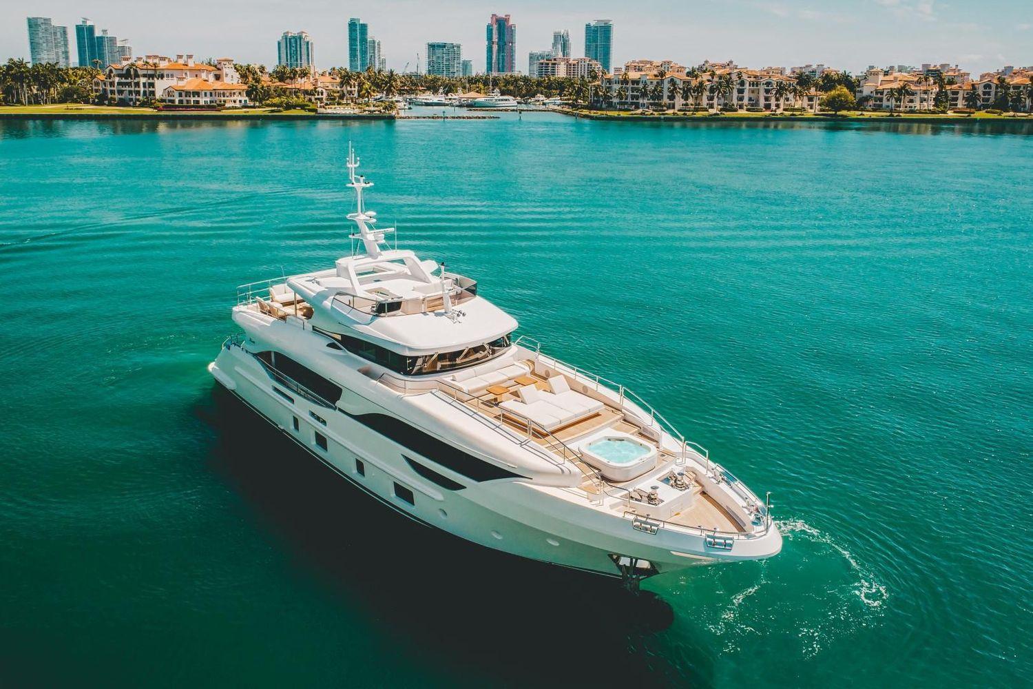 Luxurious 2020 Benetti Delfino yacht cruising in turquoise waters near a city skyline.