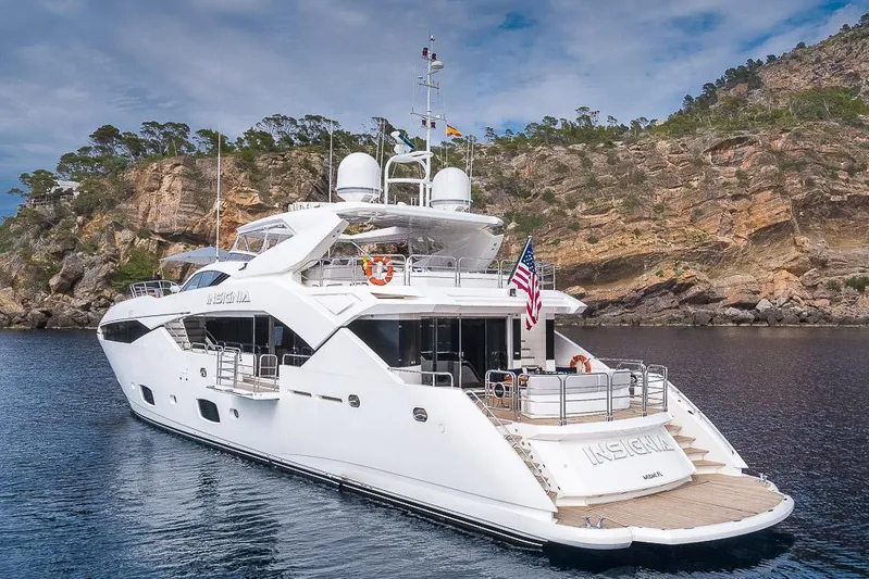 Insignia Yacht Photos Pics Luxurious 2015 Sunseeker 115 yacht anchored near rocky coastline under a cloudy sky.