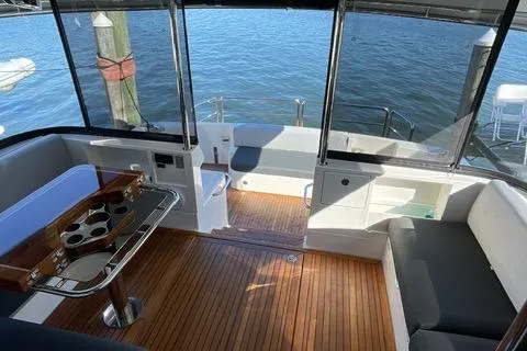  Yacht Photos Pics 2025 Riviera 585 SUV yacht interior with wooden flooring and seating, overlooking serene water.