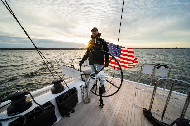 Fortitude Yacht Photos Pics Person steering CNB 66 yacht, American flag, sunset over ocean, 2021 model.