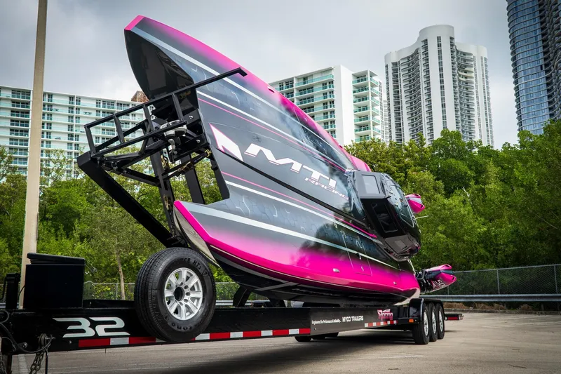  Yacht Photos Pics 2023 MTI 390XR powerboat on trailer, vibrant pink and black design, urban skyline backdrop.