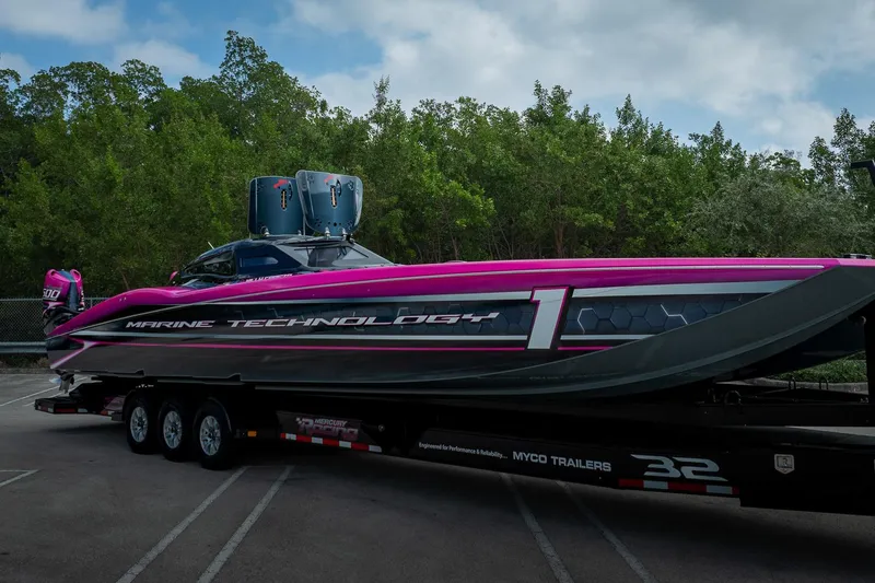 Yacht Photos Pics 2023 MTI 390XR powerboat on trailer, vibrant pink and black design, parked near trees.