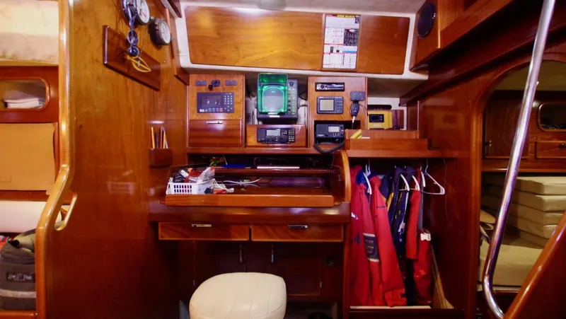 Forever Young Yacht Photos Pics Navigation station inside 2000 Amel Super Maramu yacht, featuring wooden cabinetry and electronic equipment.