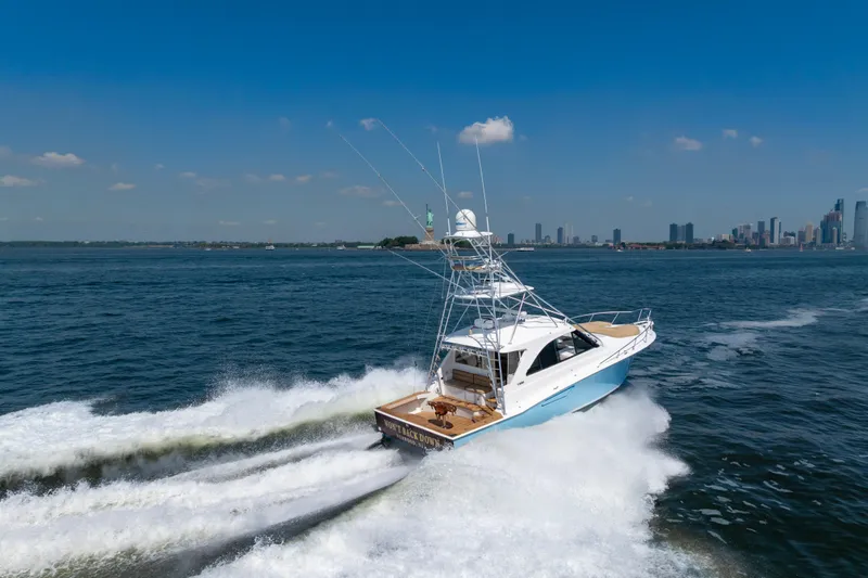  Yacht Photos Pics 2012 Cabo 44 Hardtop Express yacht cruising near city skyline on a sunny day.