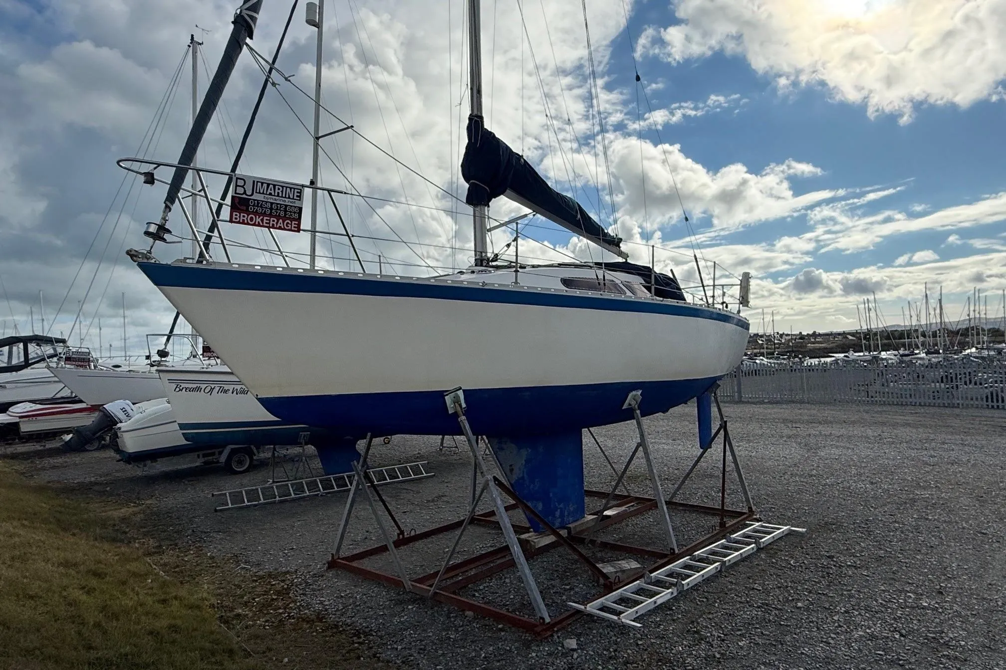 1984 Trapper T30 sailboat on stands, brokerage sign, cloudy sky background.