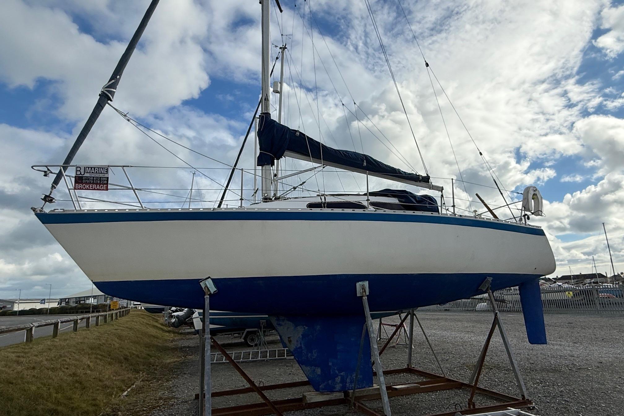 1984 Trapper T30 sailboat on dry dock under cloudy sky.