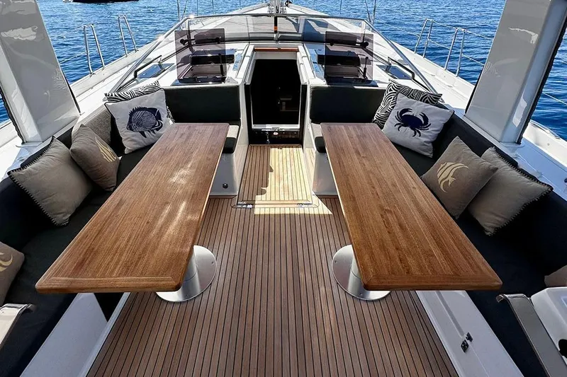 Nil Yacht Photos Pics Luxurious 2024 Hanse 588 yacht deck with wooden tables and nautical-themed cushions.