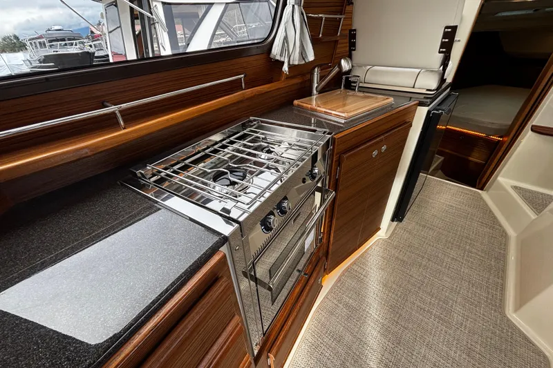  Yacht Photos Pics 2026 Ranger Tugs R-29 CB interior kitchen with stove, sink, and wooden cabinetry.
