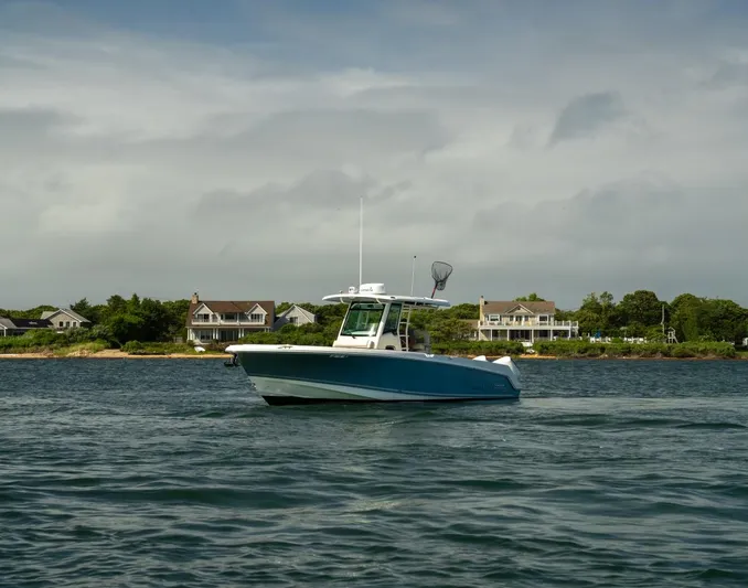 Just Wednesdays Yacht Photos Pics 2022 Boston Whaler 330 Outrage boat cruising near coastal homes under cloudy skies.