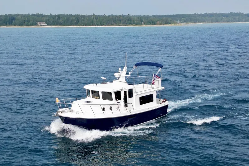  Yacht Photos Pics 2018 American Tug 365 cruising on open water near a forested shoreline.