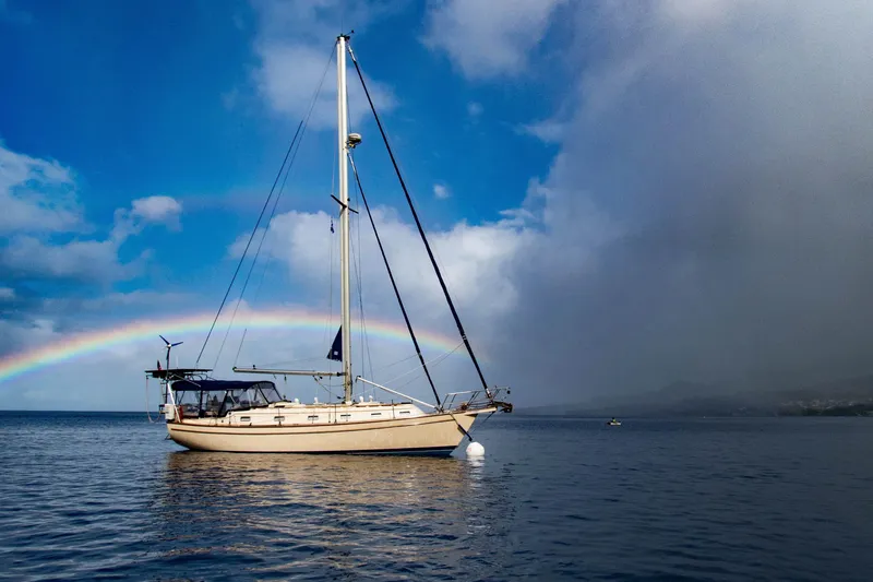 Blue Skies Yacht Photos Pics Sailboat Island Packet 40 (1995) anchored under a vibrant rainbow on a calm sea.