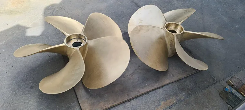 Bouki Yacht Photos Pics Two large brass boat propellers on a concrete surface, Bertram 670, 2006 model.