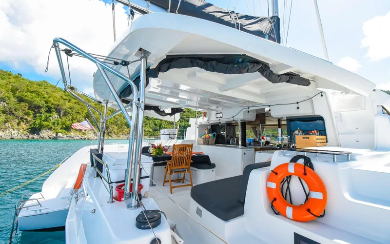 Celavie Yacht Photos Pics 2021 Lagoon 46 catamaran with spacious deck, docked by scenic shoreline.