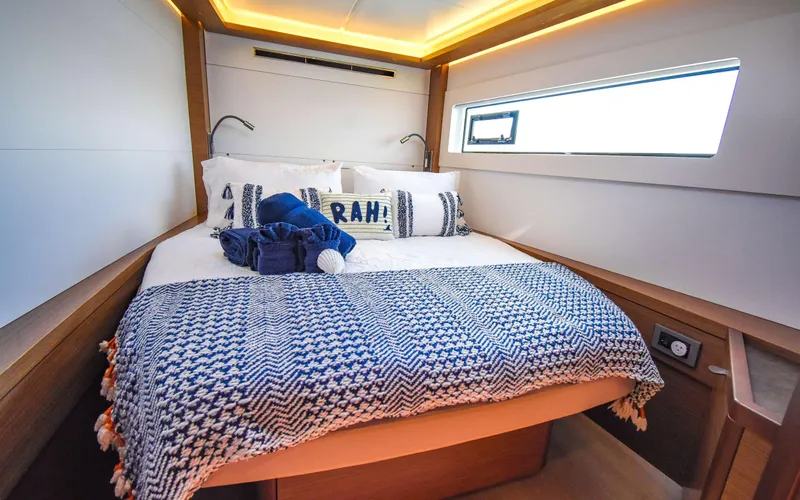 Celavie Yacht Photos Pics Luxurious bedroom interior of 2021 Lagoon 46 yacht with cozy bedding and ambient lighting.