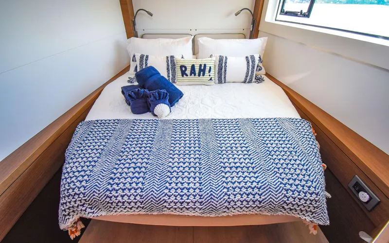 Celavie Yacht Photos Pics Cozy bedroom in 2021 Lagoon 46 yacht with nautical-themed decor and window view.